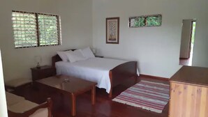 A bedroom with a bed, bedside table, and a small desk. There is a window with blinds, a framed picture on the wall, and a wooden cabinet. - Ocho Rios Pimento Villas (Ocho Rios)