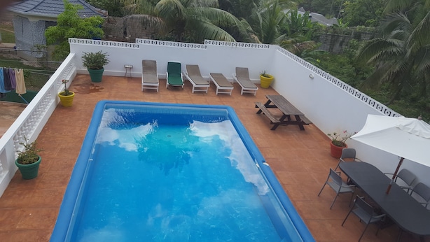 A rectangular swimming pool with a white deck surrounding it, equipped with lounge chairs and a wooden table. - Ocho Rios Pimento Villas (Ocho Rios)