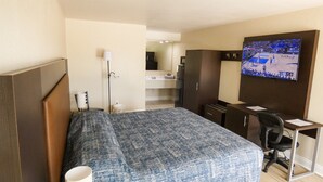 Habitación de hotel con cama, escritorio, silla, televisión, armario y baño a la vista.