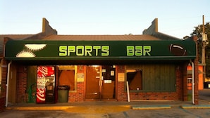 Un bar deportivo con un letrero de Coca-Cola, fachada de ladrillo y toldo verde.