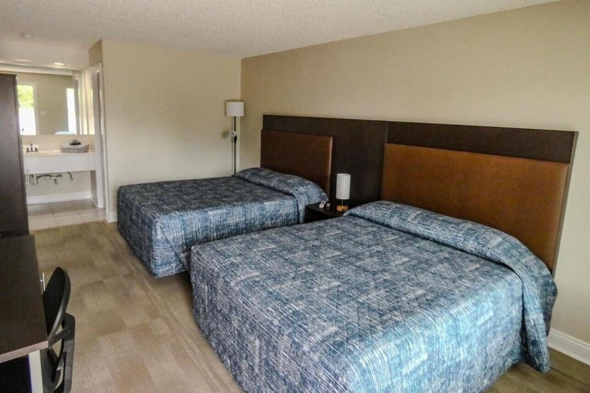 Quarto de hotel com duas camas, uma mesa e um espelho.