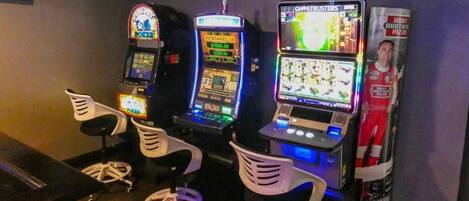 Une rangée de bornes d’arcade avec des chaises devant, une affiche accrochée au mur et un comptoir avec un menu.