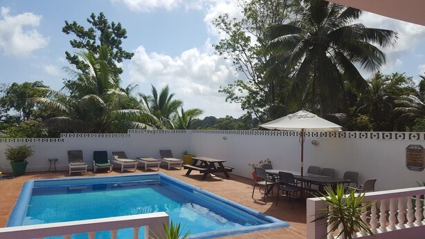 A pool area with lounge chairs and a table, surrounded by a white wall with a decorative pattern. - Ocho Rios Tamarind Villas (Ocho Rios)