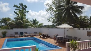 A pool area with lounge chairs and a table, surrounded by a white wall with a decorative pattern. - Ocho Rios Tamarind Villas (Ocho Rios)