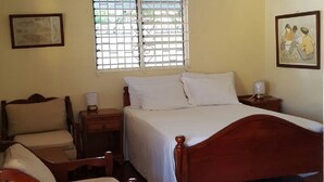 A bedroom with a wooden bed, a chair, a nightstand, a window with bars, and a ceiling fan. - Ocho Rios Tamarind Villas (Ocho Rios)