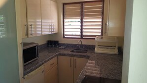 A compact kitchen with a granite countertop, a built-in sink, and a window with blinds. - Ocho Rios Cinnamon Villas (Ocho Rios)