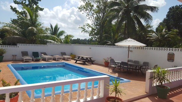 A swimming pool with lounge chairs and a picnic table, surrounded by a white fence and tropical vegetation. - Ocho Rios Cinnamon Villas (Ocho Rios)