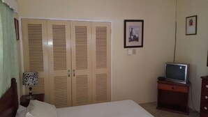 A bedroom with a bed, a wooden wardrobe, a television on a wooden stand, and a lamp. - Ocho Rios Cinnamon Villas (Ocho Rios)