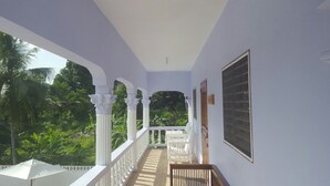 A balcony with white railings, a wooden bench, and a view of lush greenery. - Ocho Rios Cinnamon Villas (Ocho Rios)
