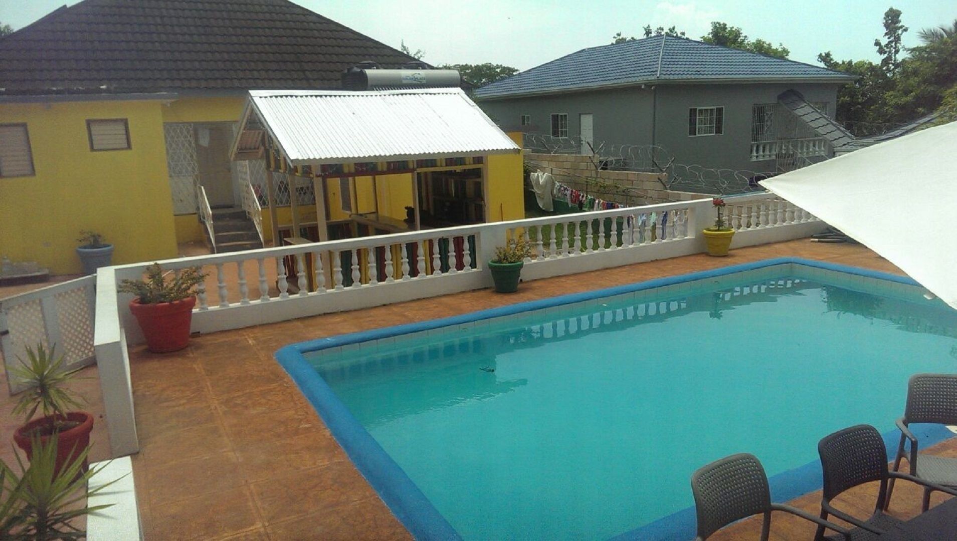 Ein Swimmingpool mit weißer Reling, umgeben von Kübelpflanzen und einer Terrasse mit Gartenmöbeln.