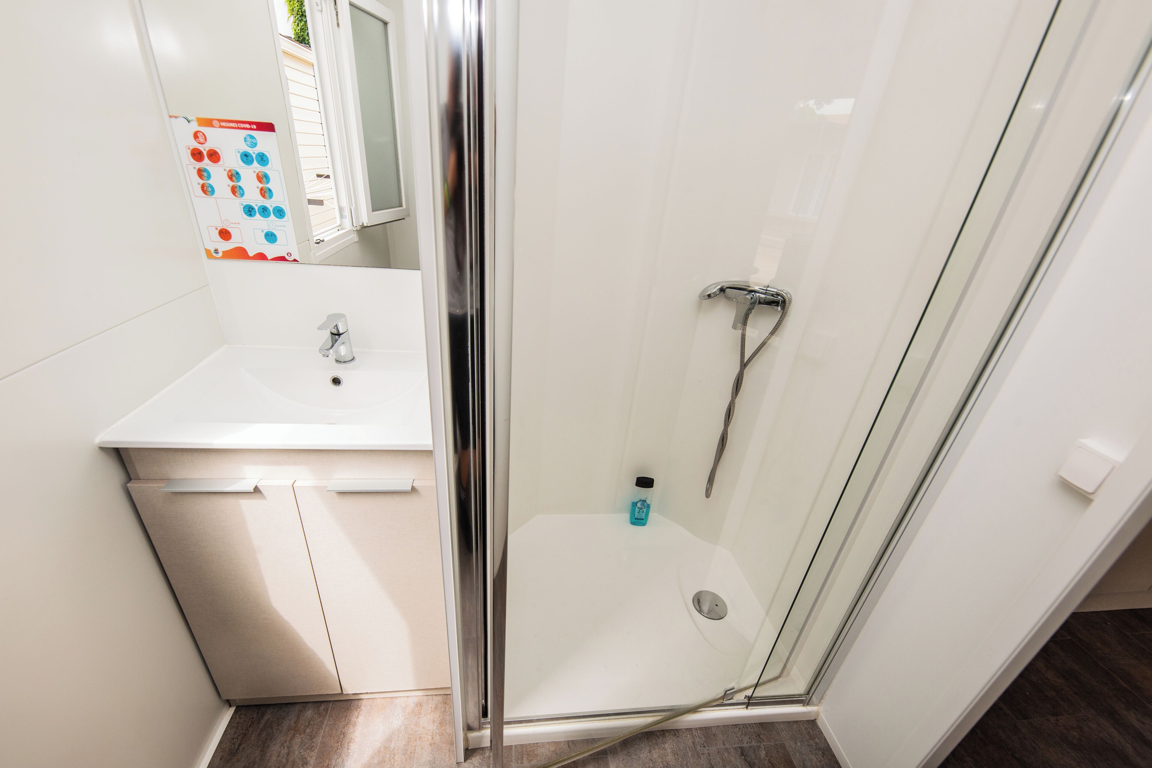 A modern bathroom with a glass shower enclosure, a white sink, and a mirror.