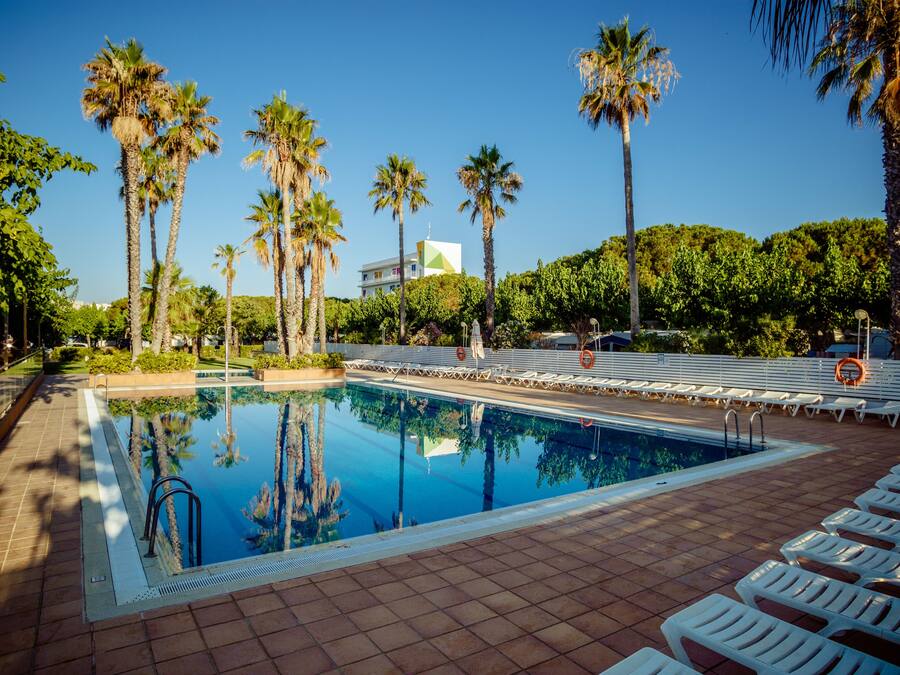 A swimming pool with lounge chairs, palm trees, and a building in the background.