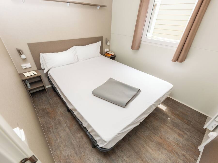 A neatly made bed with a folded blanket, a bedside table with a lamp, and a nightstand with a phone and a book.