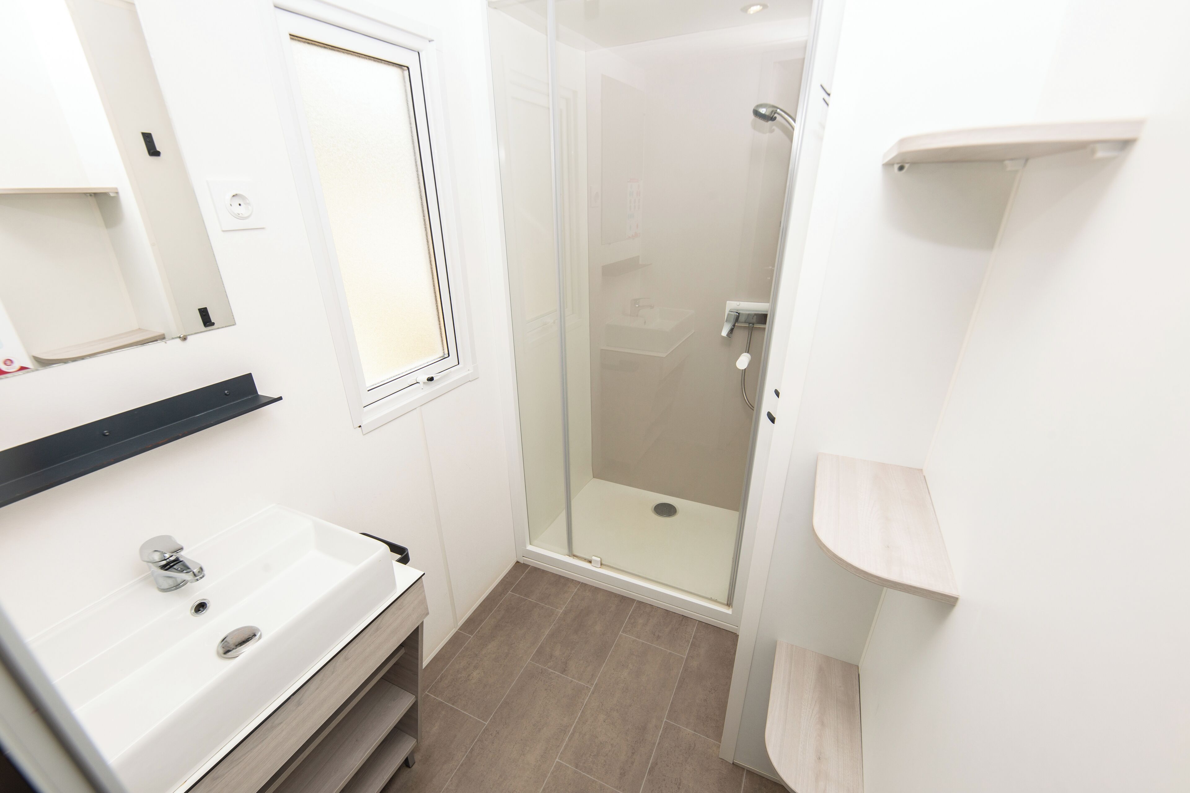 Un baño moderno con un lavamanos blanco, ducha con mampara de vidrio y tocador de madera.