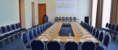 Un salón de conferencias con una larga mesa, sillas azules y una pantalla de proyector mostrando 'WAZO'.