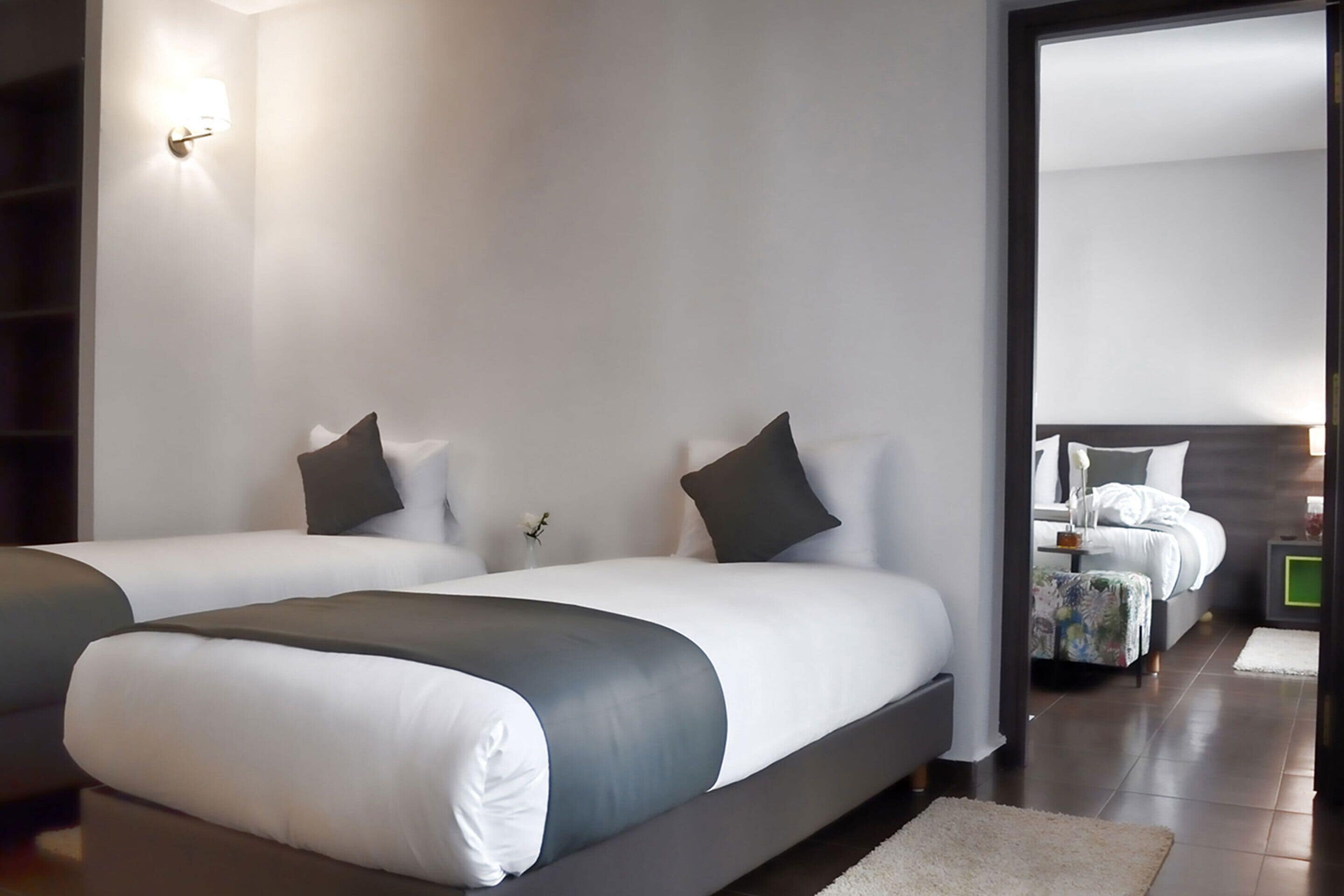Een moderne hotelkamer met twee bedden, een grote spiegel en uitzicht op een andere kamer.