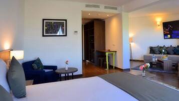 A hotel room with a bed, a sofa, a small table with a vase of flowers, a TV, and a fireplace.