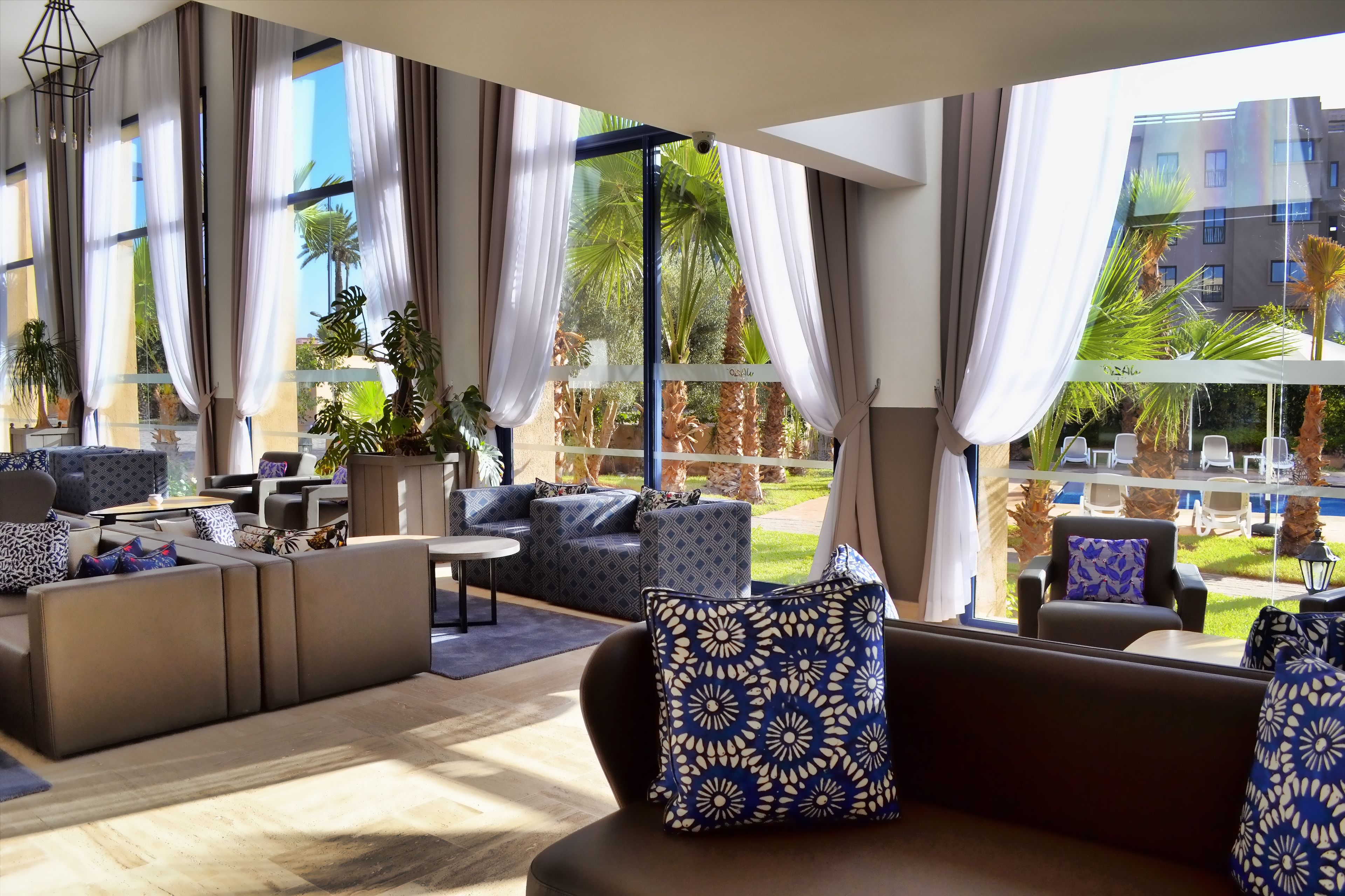 A modern lounge area with large windows, comfortable seating, and a view of a pool and greenery.
