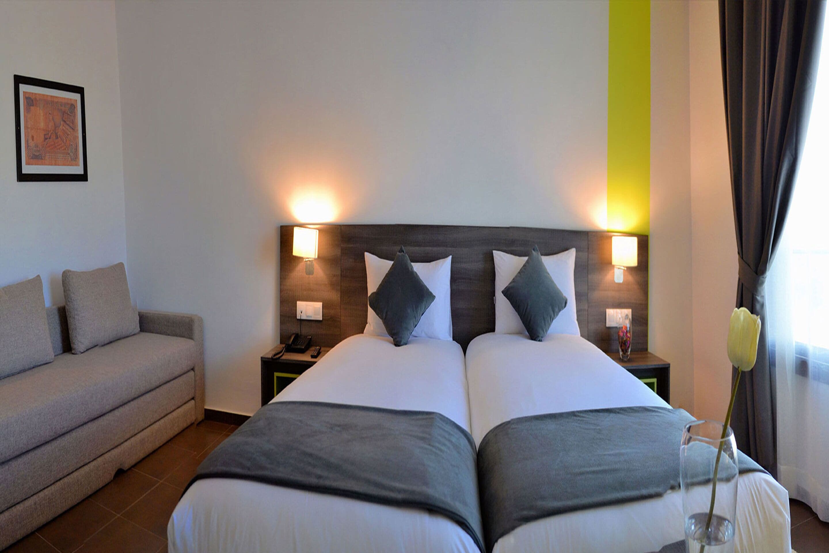Habitación de hotel con una cama doble, dos mesitas de noche, un sofá y un cuadro enmarcado en la pared.