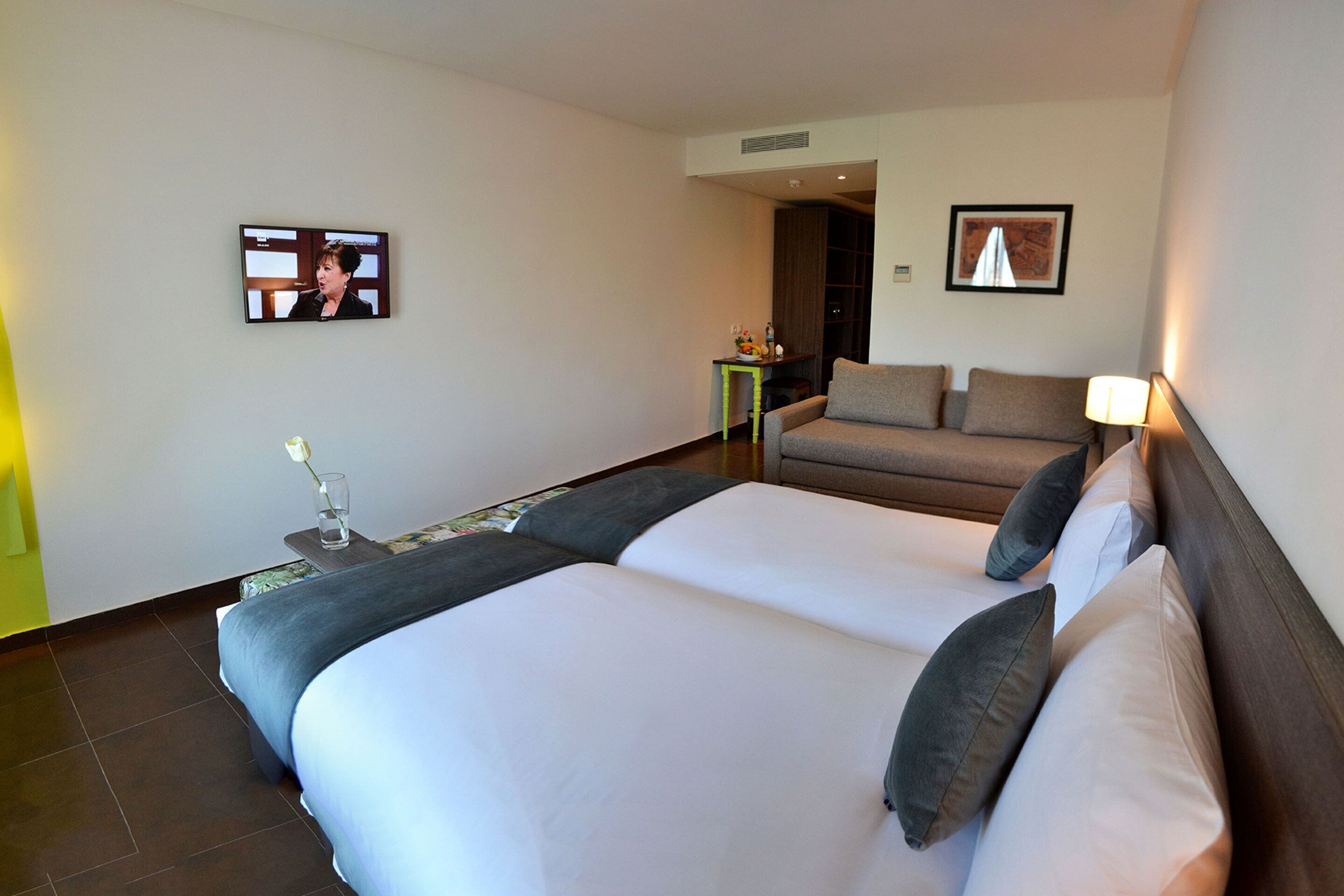A hotel room with two beds, a sofa, a TV, and a small table with a vase and flowers.