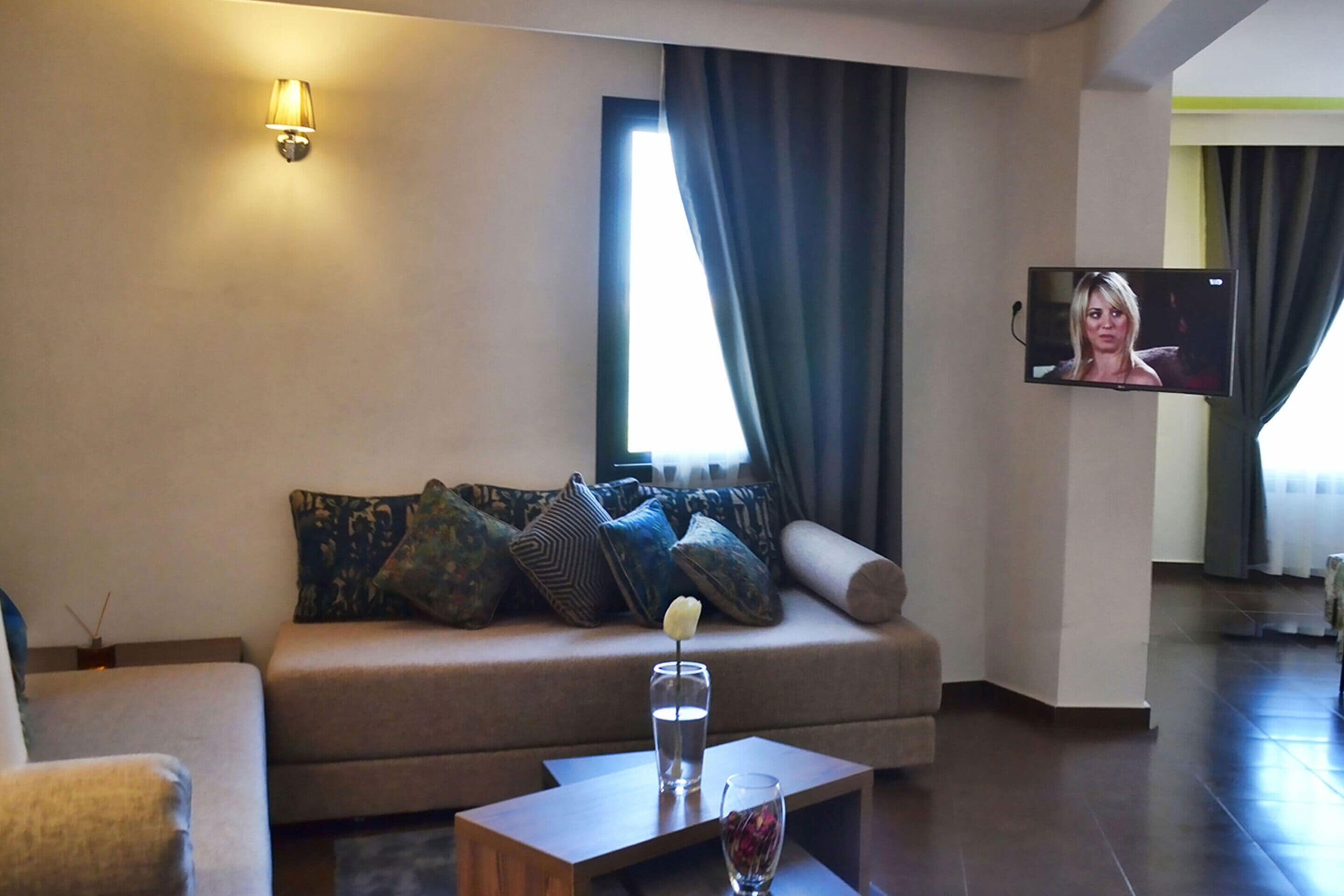 Una sala de estar moderna con un sofá, una mesa de centro, un televisor montado en la pared y una ventana con cortinas.