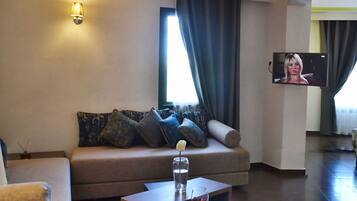 Una sala de estar moderna con un sofá, una mesa de centro, un televisor montado en la pared y una ventana con cortinas.