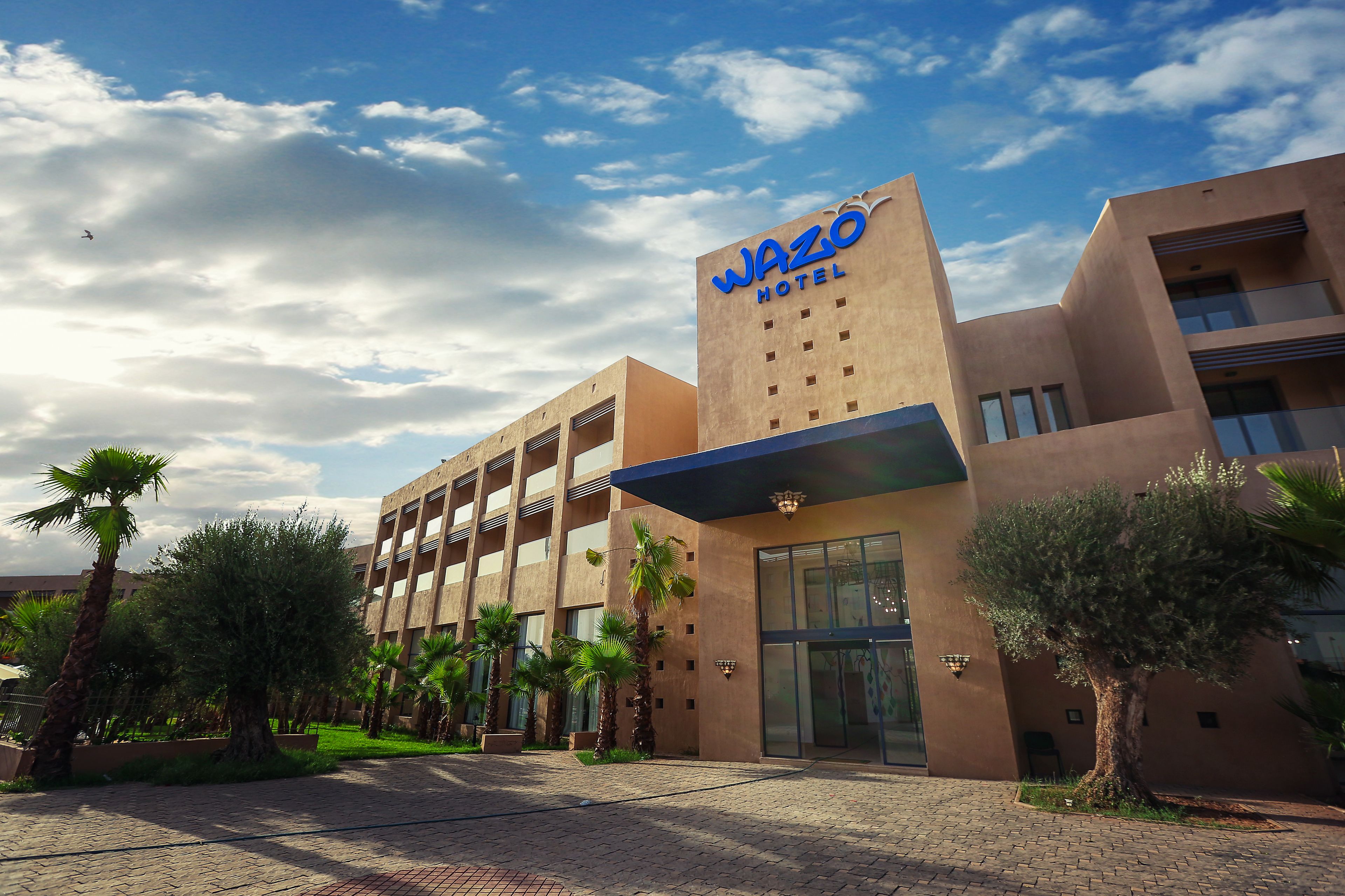 A hotel with a modern architectural design, featuring a prominent sign and a landscaped entrance area.