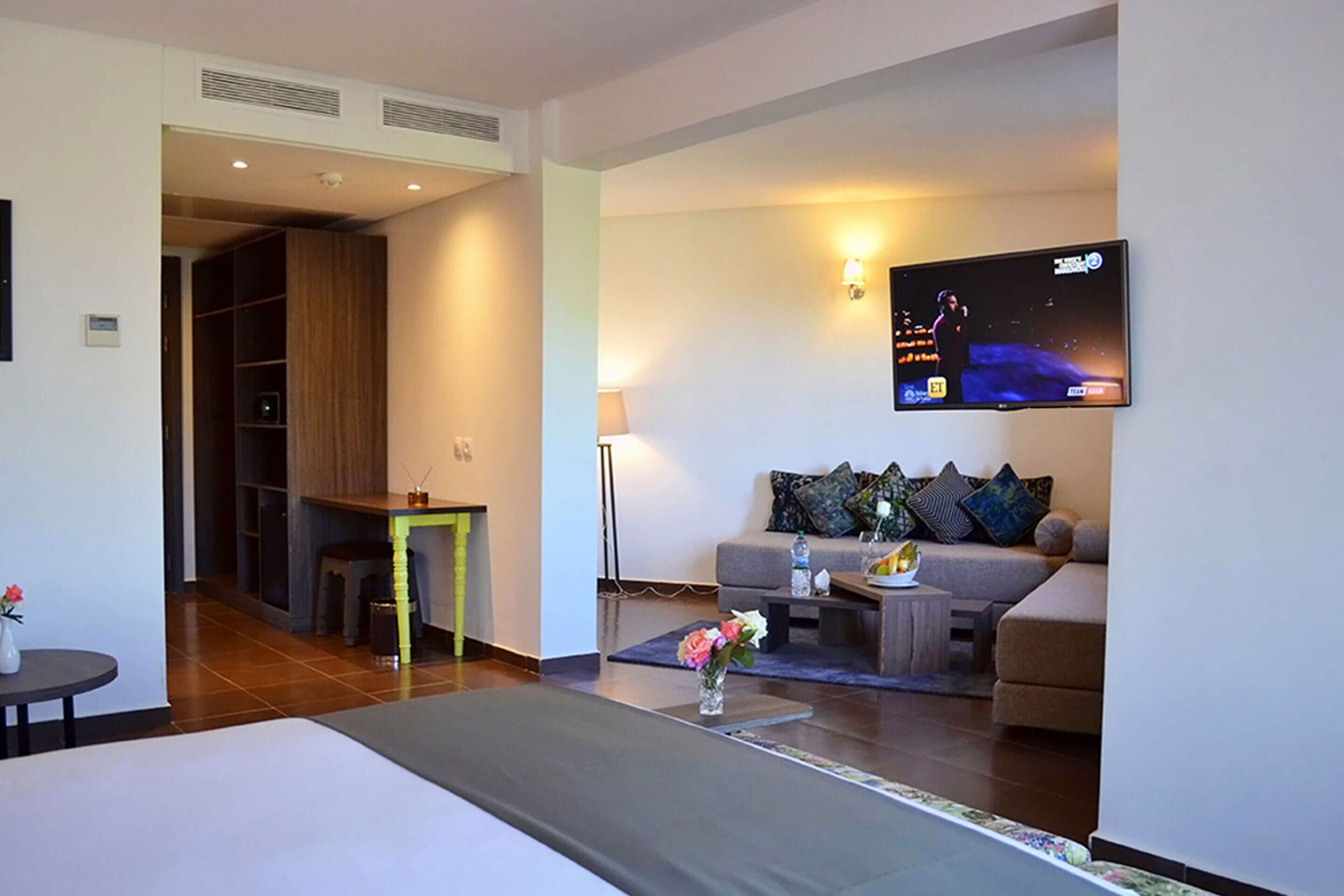 A modern hotel room with a bed, a sofa, a TV mounted on the wall, and a small dining table.