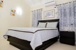 A bedroom with a bed, a nightstand, a wall-mounted air conditioner, and a framed picture.
