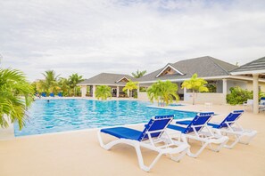 A swimming pool with blue lounge chairs and palm trees.