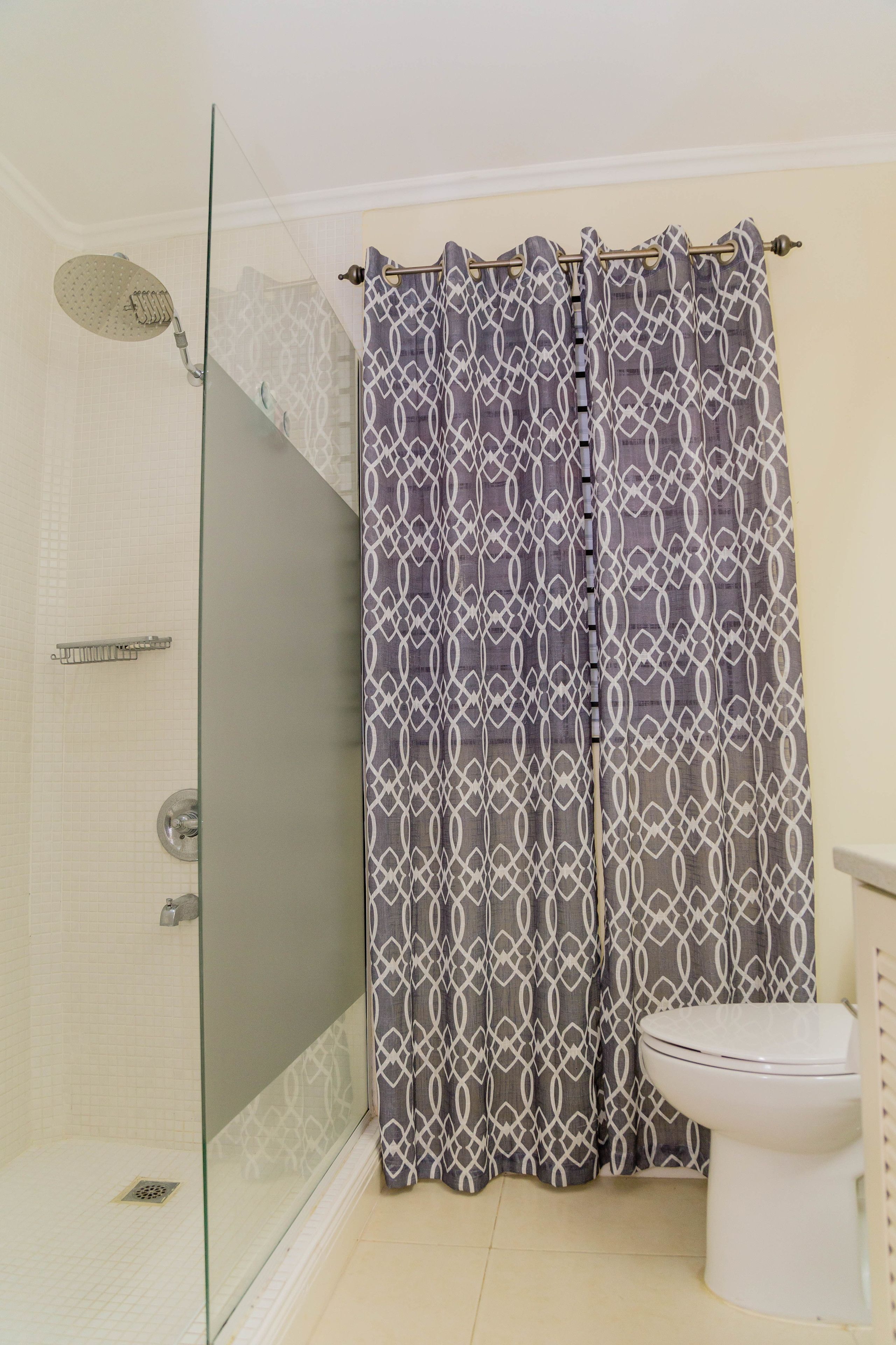 Een badkamer met een glazen douchecabine, een toilet en een douchegordijn met een patroon.