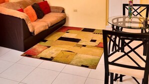 Una sala de estar con un sofá, una mesa de vidrio, un ventilador de techo y una puerta.
