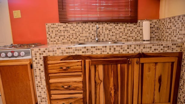Una cocina con salpicadero de azulejos, armarios de madera, una estufa y una ventana con persianas.