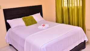 Una cama bien hecha con sábanas blancas, una almohada decorativa verde y un juego de toallas sobre la cama.