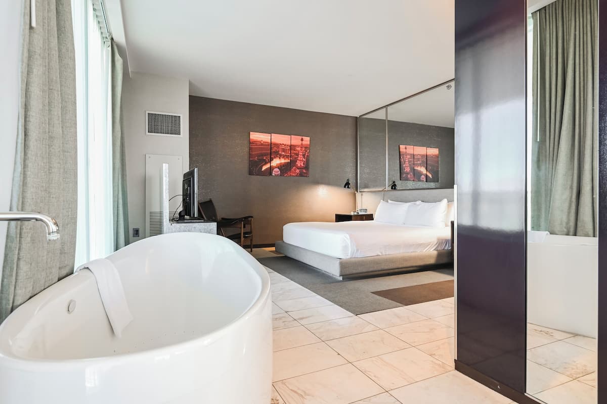 Une chambre d’hôtel moderne dotée d’une grande baignoire, d’un lit avec du linge de maison blanc, d’un téléviseur à écran plat et d’œuvres d’art accrochées aux murs.