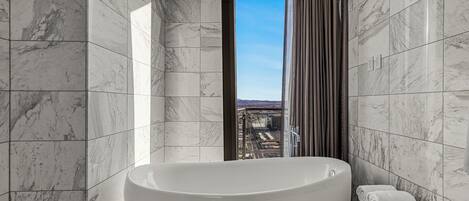 Een moderne badkamer met een vrijstaand bad, een toilet en uitzicht op een stadsgezicht door een raam.