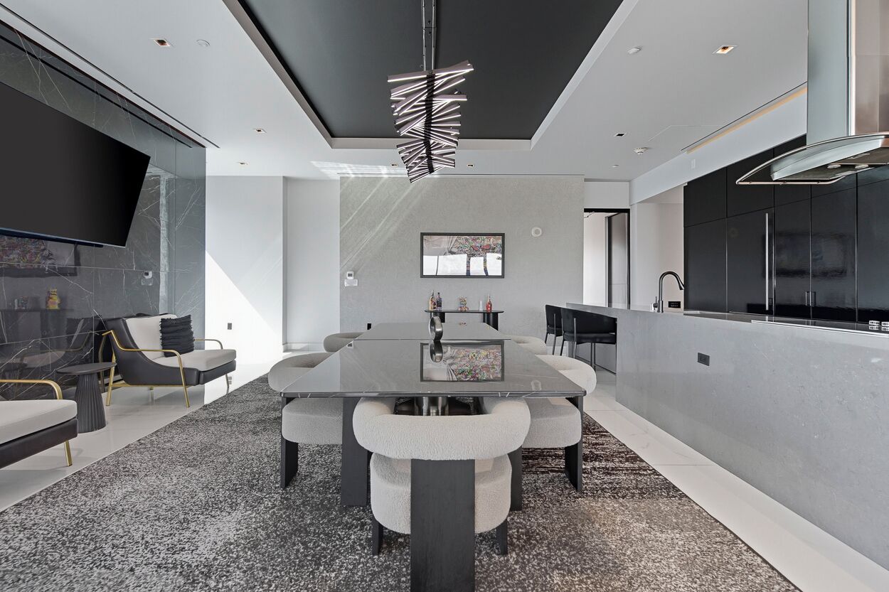 Uma sala de conferências moderna com uma mesa de vidro, assentos confortáveis, uma grande televisão de tela plana e uma copa com armários escuros.