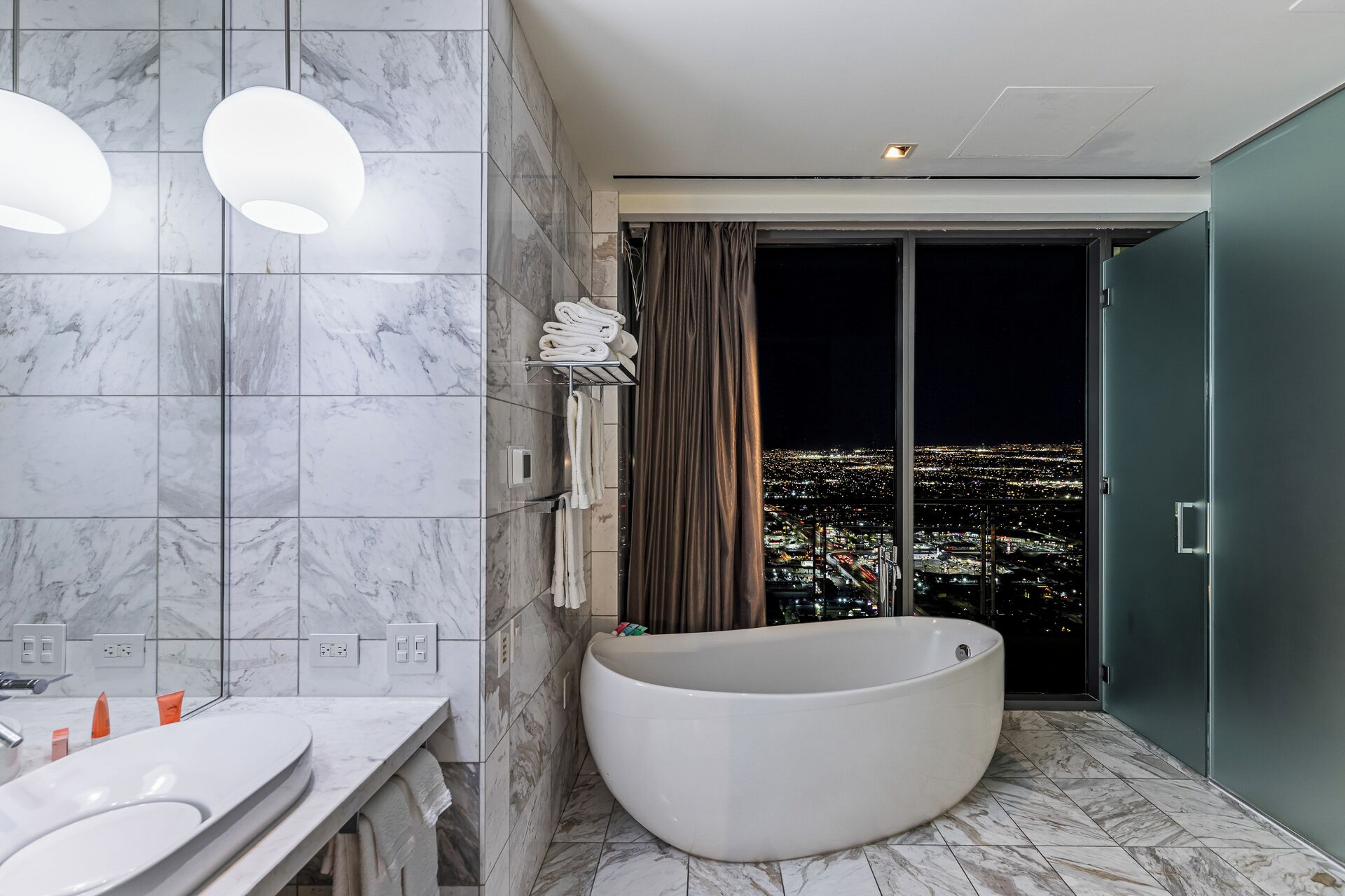 Ein modernes Badezimmer mit Badewanne, Marmorfliesen und Blick auf die Stadt.
