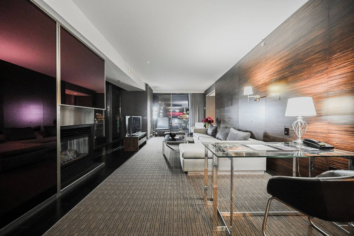 Une chambre d’hôtel moderne avec une table basse en verre, un canapé, une télévision et une cheminée.