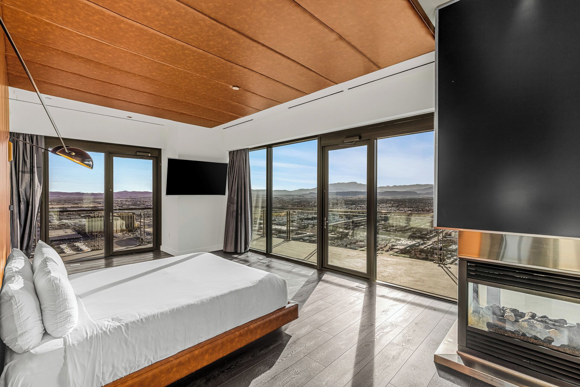 A modern bedroom with a large bed, a fireplace, and expansive windows offering a city view.