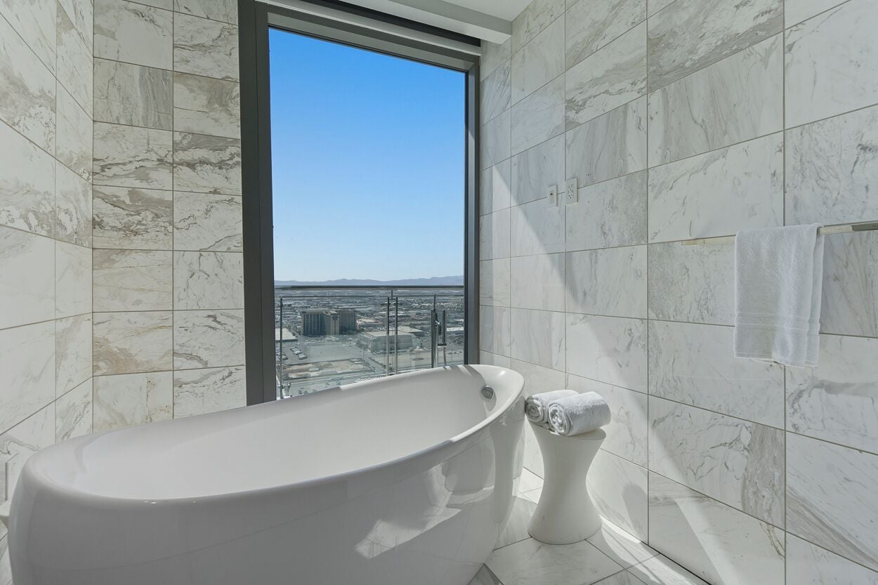 A modern bathroom with a freestanding bathtub, a toilet, and a large window offering a city view.