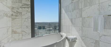 A modern bathroom with a freestanding bathtub, a toilet, and a large window offering a city view.