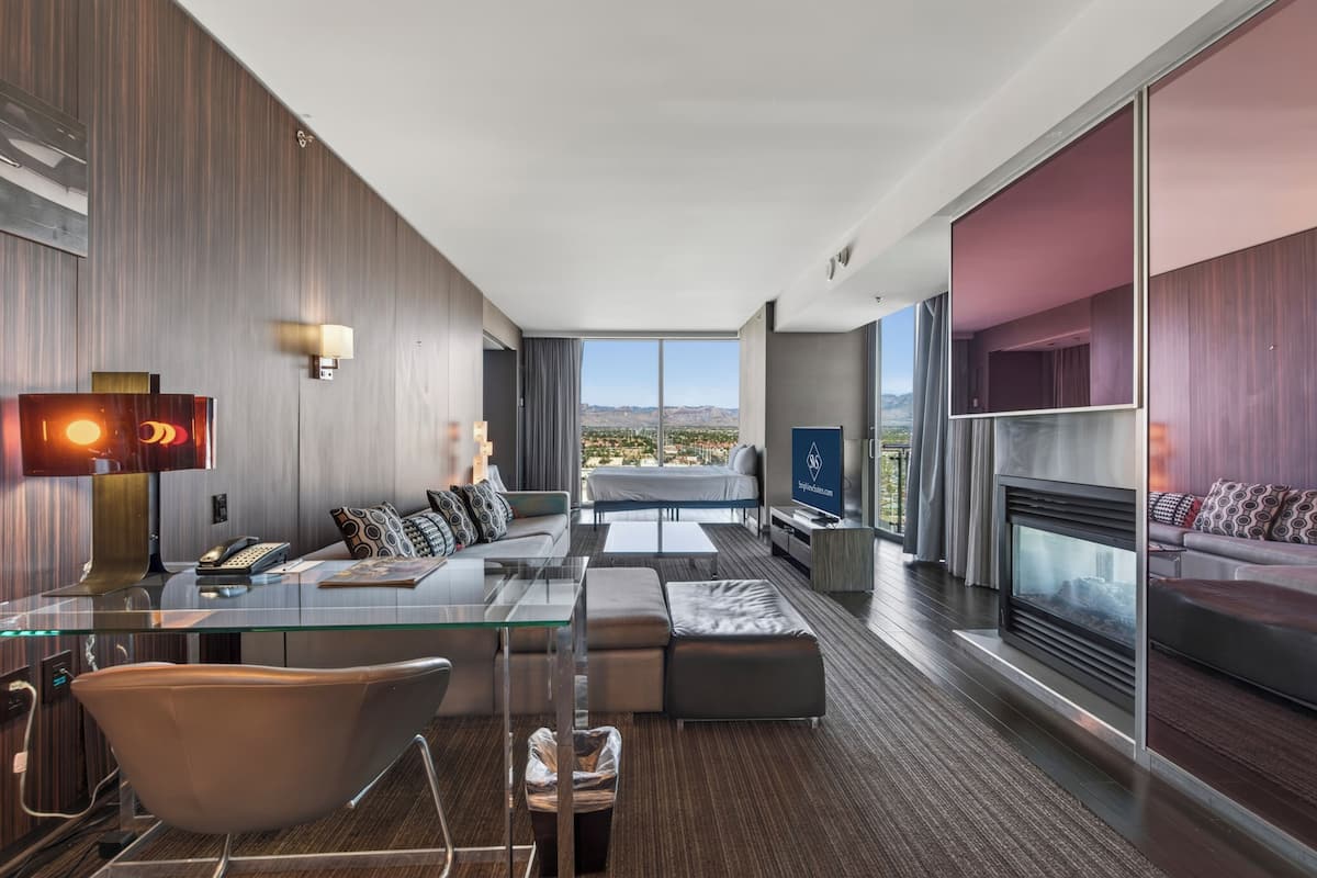 Une chambre d’hôtel moderne avec un bureau en verre, un canapé et une cheminée.