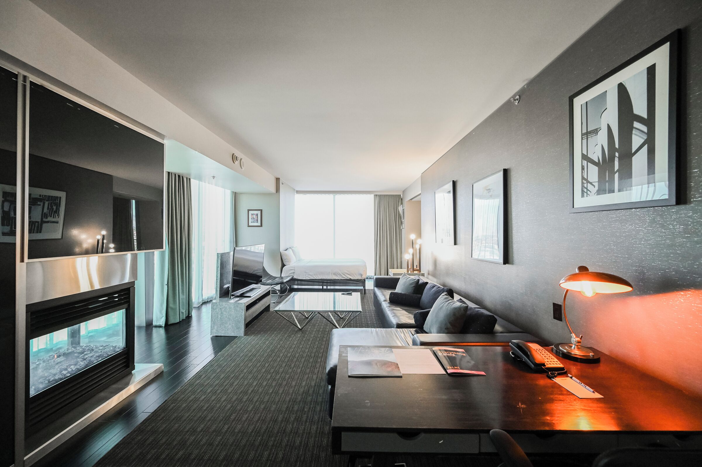 Una habitación de hotel moderna con sofá, escritorio con lámpara, chimenea y obras de arte enmarcadas en las paredes.