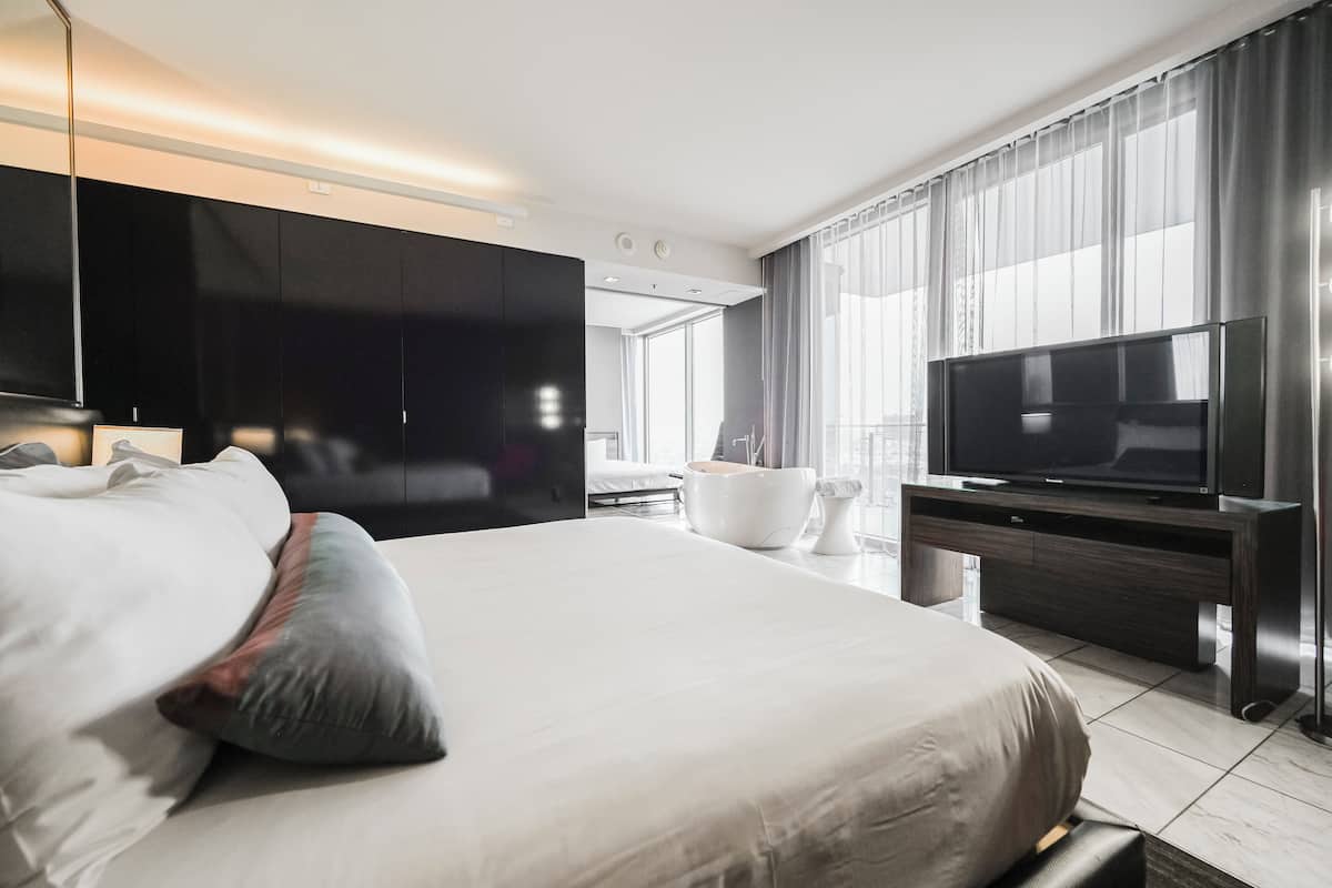 Une chambre d’hôtel moderne dotée d’un grand lit, d’un téléviseur à écran plat et d’une grande fenêtre avec des rideaux.