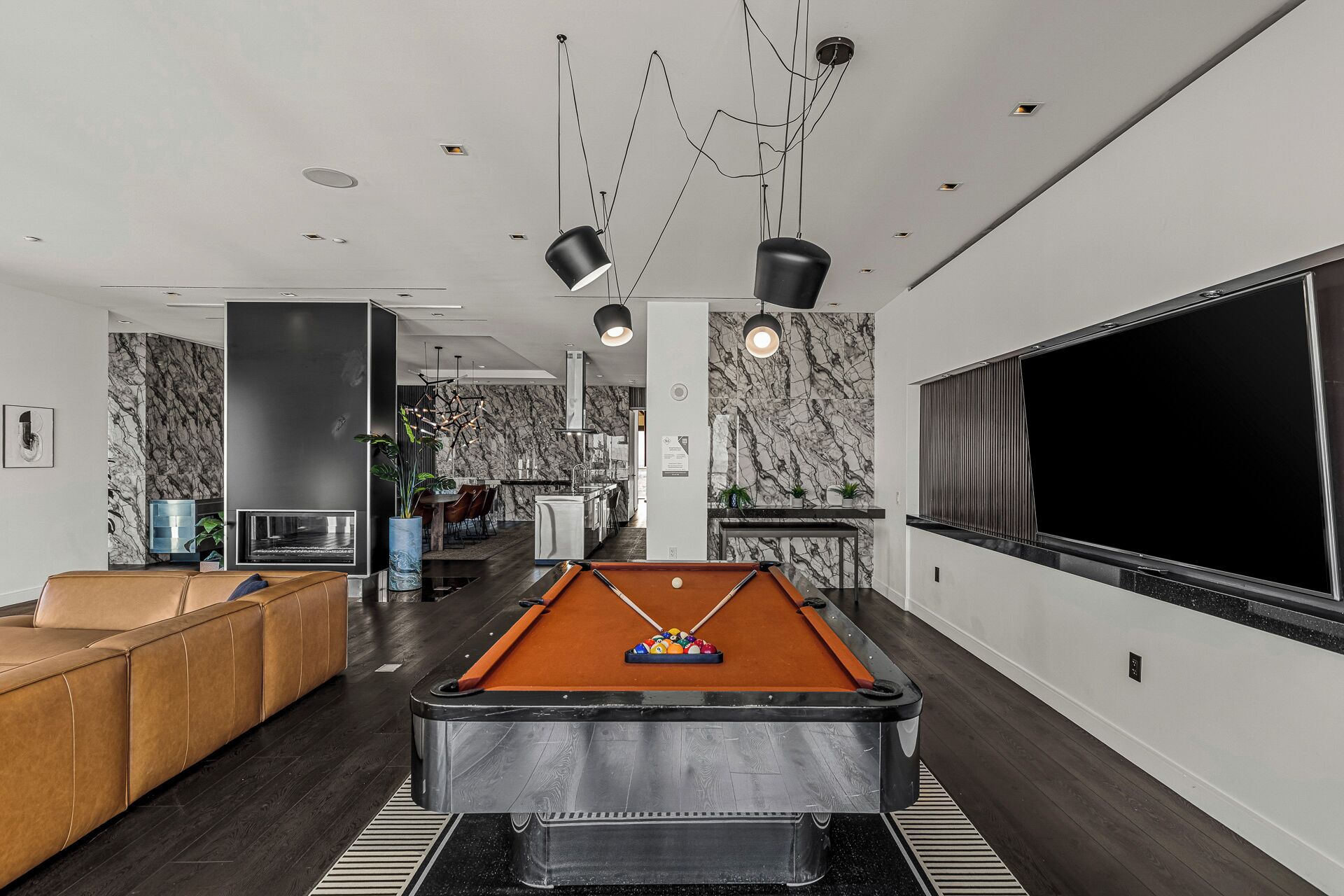 Een moderne woonkamer met een pooltafel, een bank en een groot televisiescherm.