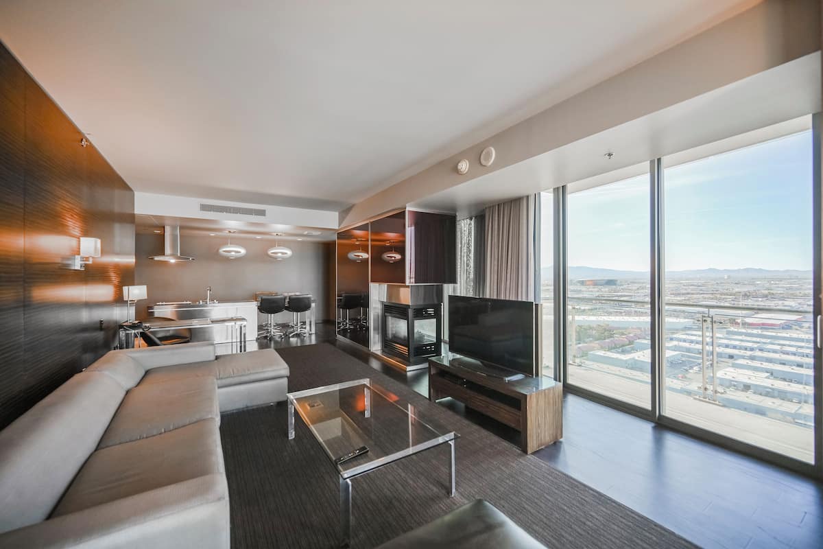 Une chambre d’hôtel moderne dotée d’une grande télévision, de sièges confortables, d’un coin cuisine et offrant une vue sur la ville.