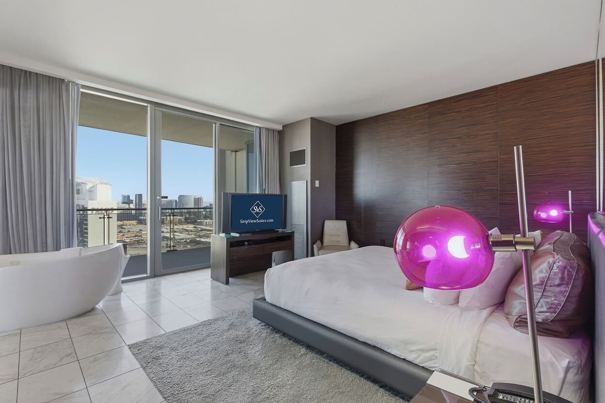 Une chambre d’hôtel moderne dotée d’un grand lit, d’une baignoire, d’un téléviseur à écran plat et offrant une vue sur la ville.