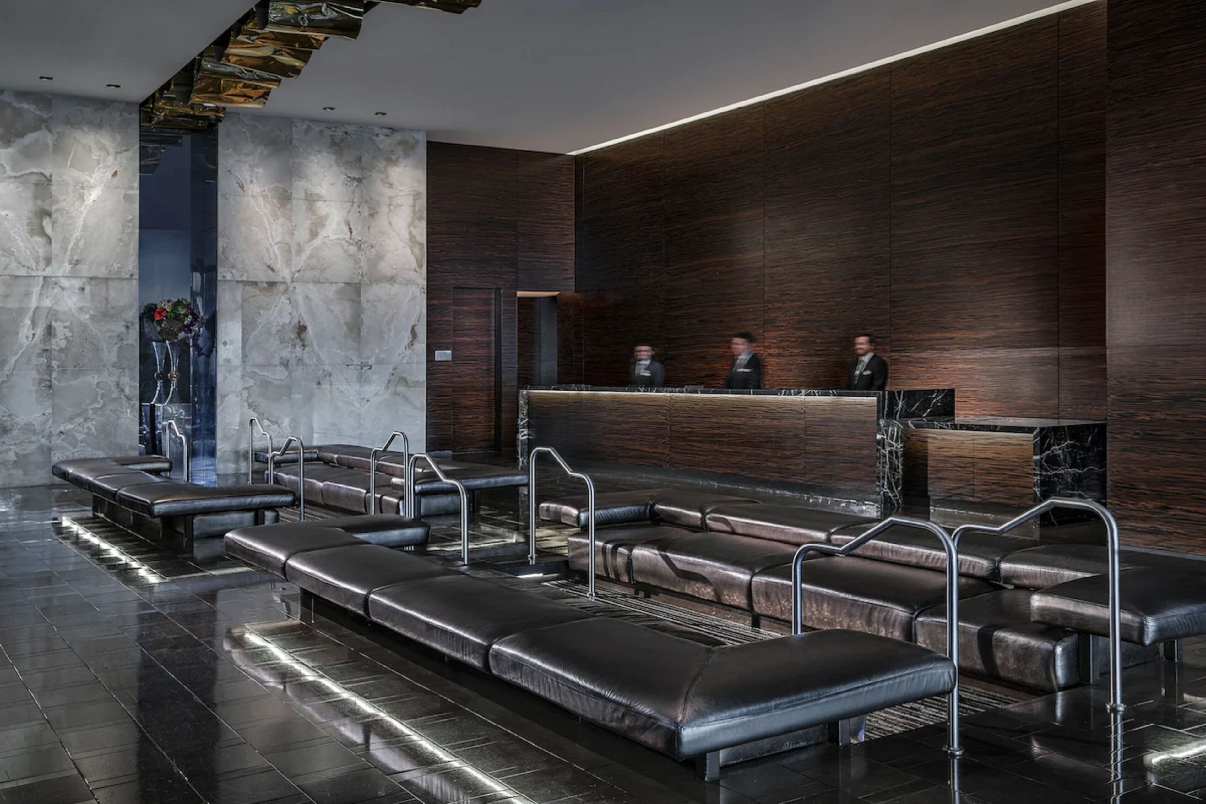 Un hall d’entrée moderne avec des sièges en cuir, un comptoir d’accueil et des murs en marbre.