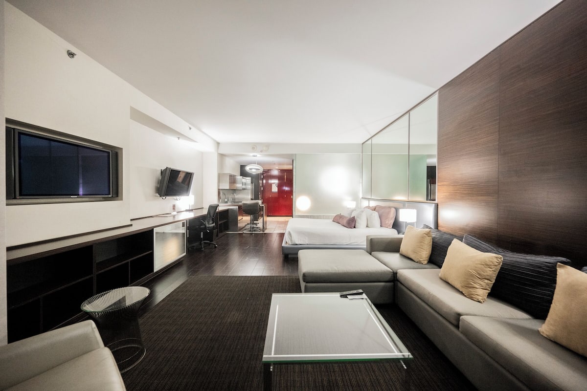 Une chambre d’hôtel moderne équipée d’un grand lit, d’un canapé, d’une télévision, d’un bureau et d’un miroir.